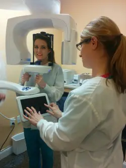 The image shows a dental professional interacting with a digital X-ray machine in a dental clinic