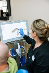 A dental professional wearing blue gloves is using a computer monitor to review or analyze a digital image of a tooth or dental structure. 